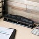A black Universal 2 or 3 hole punch on a countertop near a calculator and paper.