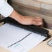 A person using a Universal black countertop hole punch to punch paper at a table.