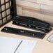 A black Universal countertop 2 or 3 hole punch on a wood surface next to a calculator and stapler.