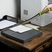 A hand with a green Swingline paper cutter trimming paper on a table.