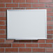 A Universal deluxe white melamine dry erase board on a brick wall.