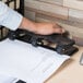 A person using a Universal black countertop power assist 3 hole punch to punch a piece of paper.