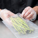 A person in gloves holding an ARY VacMaster chamber vacuum packaging bag of asparagus.