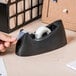 A hand using a Universal black tape dispenser on a desk.