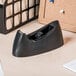 A black Universal tape dispenser on a wood desk.