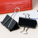 A pair of black Universal large binder clips sitting on a white surface.
