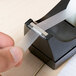 A hand using a Universal clear tape dispenser to tape a piece of paper.