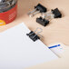 A black Universal mini binder clip on a stack of paper.