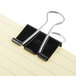 A black Universal medium binder clip on a piece of paper.