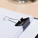A Universal black medium binder clip attached to a notebook.