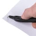 A person using a black Universal Wand Style Staple Remover to remove a staple from paper.