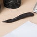 A Universal black wand style staple remover on a wood desk next to paper and office supplies.