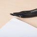 A black Universal Wand Style Staple Remover on a wood surface.