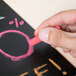 A hand holding a pink piece of Crayola drawing chalk on a blackboard.