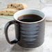 A Tuxton TuxTrendz Lava China mug filled with coffee next to a cookie.