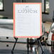 A black steel Universal portable tabletop easel holding a white paper with black text on a table.
