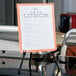 A Universal black steel portable tabletop easel with a paper menu on it.