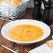 A Tuxton TuxTrendz bright white china soup bowl on a table with bread and salt and pepper.