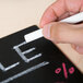 A person writing on a blackboard with white Crayola chalk.