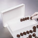 A hand in a glove holding chocolates in a Valentine's Day candy box.