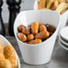 A Tuxton TuxTrendz white china bowl filled with brown food on a table.