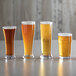 A group of Acopa Pilsner glasses of beer on a table.