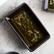 A Tuxton TuxTrendz lava china sauce dish filled with green liquid on a counter.