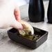 A person holding a piece of bread dipping it into a Tuxton Lava China sauce dish.