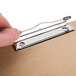 A hand using a Universal brown hardboard clipboard with a metal clip.