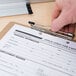 A hand using a Universal brown hardboard clipboard to fill out a paper form.