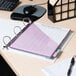 A white Avery Durable View Binder with purple paper and a pen on a desk.