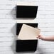 A person hanging a file in a Universal black plastic wall file.