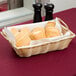 A rectangular woven basket with handles filled with bread on a table.