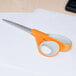 Fiskars 8" Softgrip scissors with a white and orange handle cutting a white piece of paper.