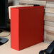 A red Universal economy non-stick binder with round rings on a wood surface.