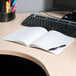 A Universal black college ruled composition notebook and pen on a desk with a computer.