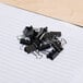 A pile of black Universal mini binder clips on a notebook.