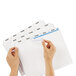 A person's hands using a blue marker to write on a white sheet of paper.
