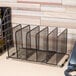 A Universal black metal mesh 5 section stacking sorter on a wood desk.