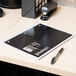 A Universal black spiral bound notebook on a desk next to a pen.
