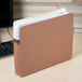 A brown Universal letter size file pocket sitting on a desk with papers in it.