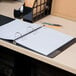 A black Universal 3 subject spiral notebook on a desk with a pen and pencil.