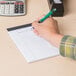 A hand holding a pen and writing on a Universal white legal writing pad.