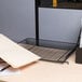 A black Universal stackable mesh tray on a desk with a computer and a folder.