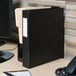 A black Universal non-view binder with a white label on the spine sits on a desk.
