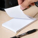 A person's hand holding a Universal white scratch pad.