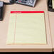 A Universal yellow legal pad with red trim on a desk.