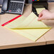 A hand holding a yellow lined Universal legal pad on a desk.