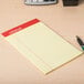 A Universal narrow ruled yellow writing pad on a wood surface with a pen and calculator.