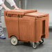 A person pushing a brown Cambro mobile ice bin.